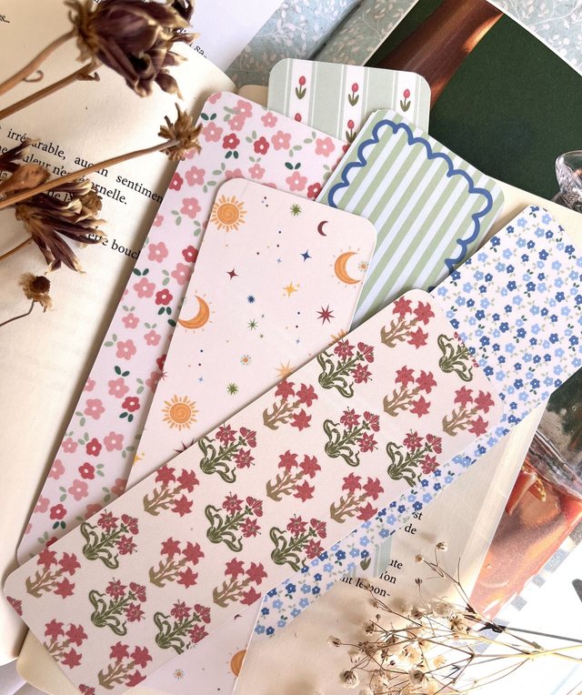 Marque-pages illustrés Iventyo posés sur des livres avec des fleurs séchées