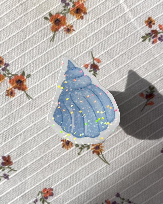 Sticker coquillage bleu pailleté posé sur une nappe à fleurs