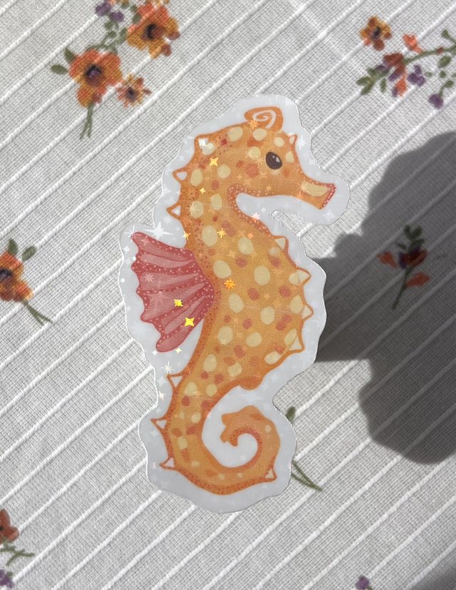 Sticker hippocampe orangé pailleté posé sur une nappe à fleurs