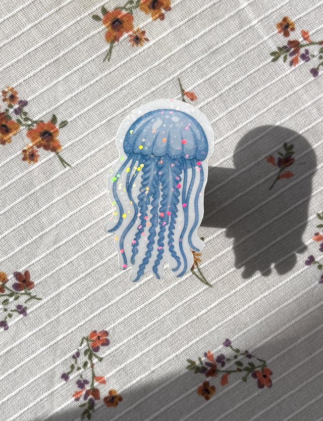 Sticker méduse bleue pailletée posé sur une nappe à fleurs