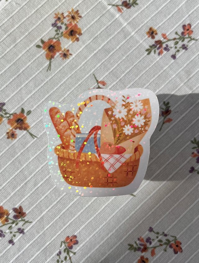 Sticker panier de pique-nique pailleté avec baguettes et fleurs sur une nappe fleurie