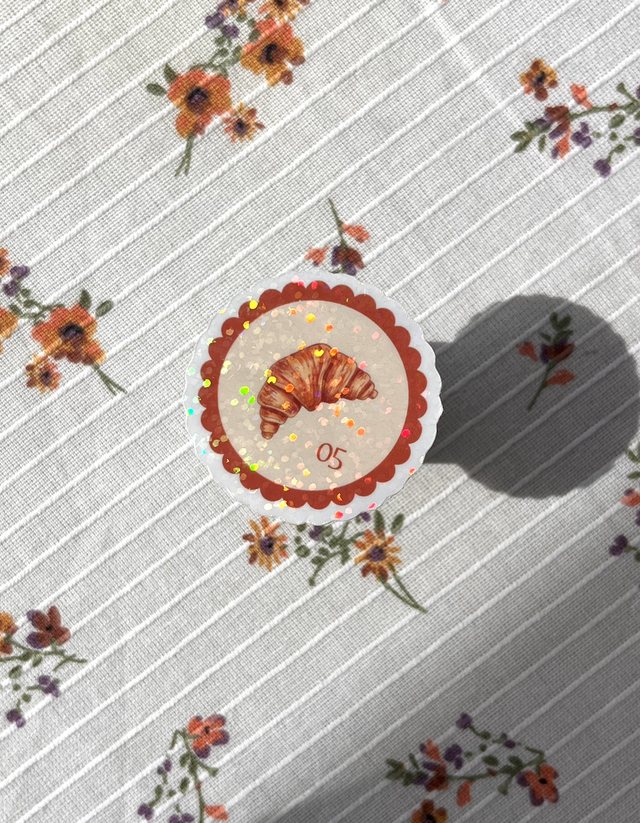Sticker timbre croissant pailleté à bord dentelé sur une nappe à fleurs