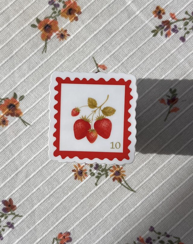 Sticker timbre fraises à bordure dentelée rouge posé sur une nappe à fleurs